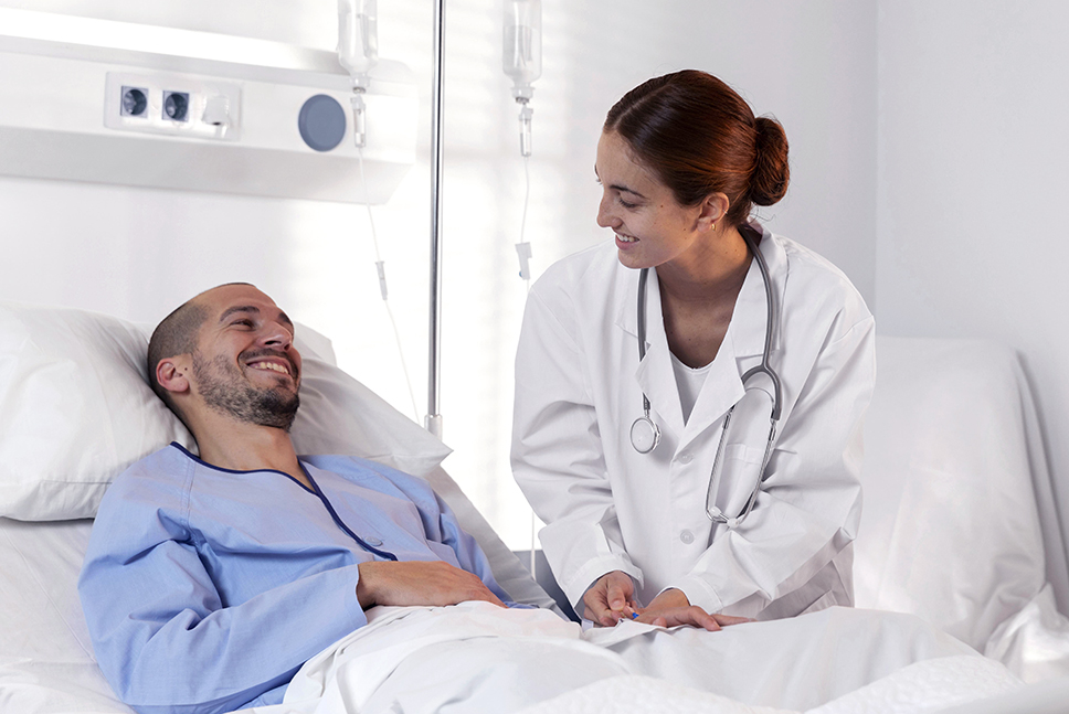 Homem sorridente internado deitado em posição semi- fowler na cama do hospital recebendo acompanhamento médico prioritário e humanizado